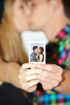 Hands, photograph and a couple kissing closeup in a booth at a party for love, celebration or romance. Happy, memory or dating with a man and woman holding a picture together closeup at an event