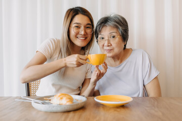 Obraz na płótnie Canvas Asian old woman mother and daughter smiling and looking at camera, one holding coffee cup and giving to mom drinking, spending time together in cafe, happy good life.