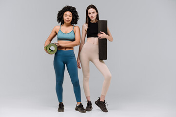 Fototapeta premium Two women in sportswear wiht yoga mat standing on gray copy space background