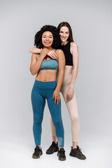 Happy friends in activewear standing together in gym isolated on gray background