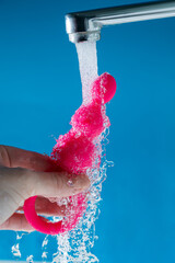 Fototapeta premium Woman holding pink anal beads under running water on blue background. Sex toy hygiene concept.