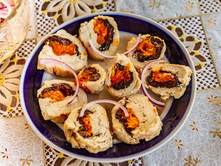 Cut pieces of a roll with chicken, prunes and dried apricots in close-up on a ceramic plate against the background of a plastic tablecloth