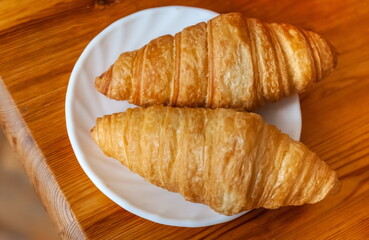Croissants on a white ceramic plate close-up against the background of a wooden kitchen table