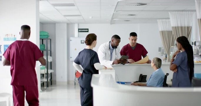 Diverse doctors discussing work, using tablet at reception desk at hospital, slow motion