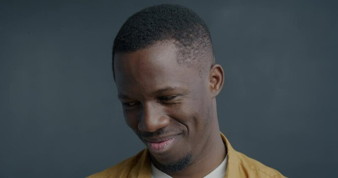Close-up slow motion portrait of shy African American man looking at camera making eyes feeling modest on grey color background. People and face expression concept.
