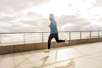 The trainer is a man active fitness every day outdoors. Full-length man warm-up in running shoes, correct technique beautiful running panorama.