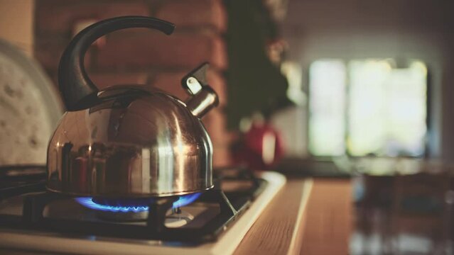 Kettle on the Gas Stove Steaming. Old tea kettle boiling in the morning in wooden off-grid cabin or chalet, close up. Steam comes out in gentle light of sunrise. Cozy morning at home kitchen. 