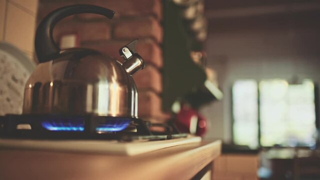 Kettle on the Gas Stove Steaming. Old tea kettle boiling in the morning in wooden off-grid cabin or chalet, close up. Steam comes out in gentle light of sunrise. Cozy morning at home kitchen. 