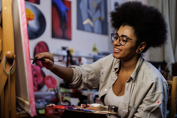 Cheerful african american artist painting on canvas in art workshop