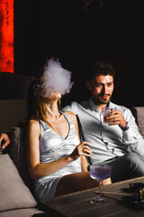 A couple in love drinks a cocktail and smokes a hookah on the terrace at night. Nightlife concept