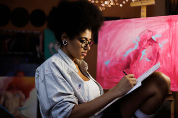 Professional african american artist in eyeglasses drawing on sketchbook in workshop