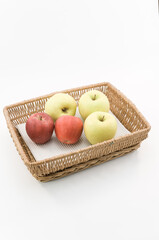 immagine primo piano di cesto in vimini con mele mature da agricoltura biologica su superficie bianca