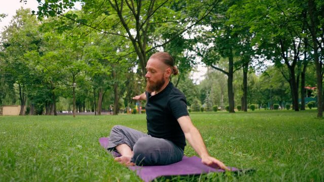 handsome bearded man meditating in the park practicing yoga doing stretching and exercises for different muscle groups