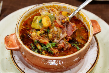 eating of traditional soup Chanakh in ceramic pot, lamb stew with tomatoes, aubergines, potatoes, greens and garlic in local restaurant