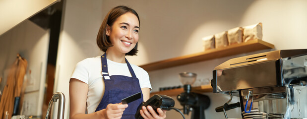Cute asian girl, barista in cafe processing contactless payment, insert credit card into POS terminal, taking order in cofee shop - obrazy, fototapety, plakaty