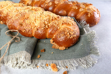 A macro shot of two challah breads topped with almond and sweet crumble on a blue cloth, angle shot.