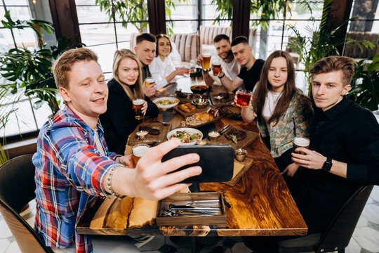 Group of happy friends making selfie photo on smartphone and drinking beer in pub restaurant