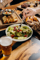 Close up of male hands eating fresh tasty salad in restaurant during dinner with friends