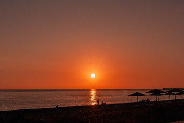 Romantic colorful sunset on the sea. Silhouettes of people and beach umbrellas against the sun down background