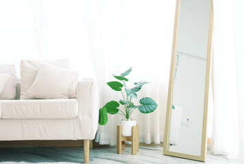 Simple white sofa With cloth pillows in the living room Decorated with green houseplants and a wooden framed mirror. Behind it is a translucent curtain. Natural light shines through making it bright