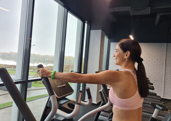 Beautiful young lady using the elliptical trainer in gym in positive mood