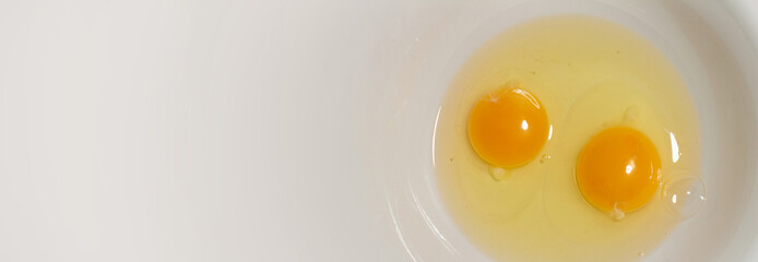 Top view. Two yellow raw fresh egg yolks and in a white plate. Horizontal banner with copy space for recipe text. Concept of healthy food, cooking in the kitchen. Copyspace. Happt easter background - obrazy, fototapety, plakaty