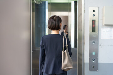 エレベーターに乗る女性 - obrazy, fototapety, plakaty