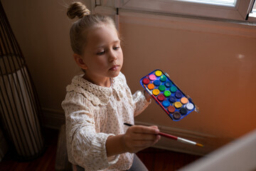 little cute girl draws with paints on canvas at the easel