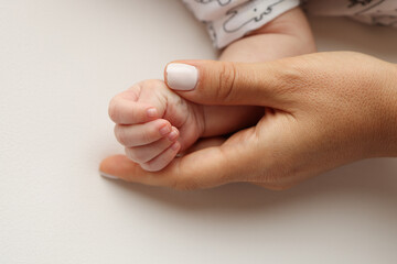 Parents' hands hold the fingers of a newborn baby. The hand of a mother and father close-up holds the fist of a newborn baby. Family health and medical care. Professional photo on white background