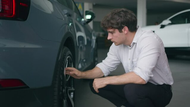 Caucasian man buyer client shopper in automobile salon male businessman choose new auto transport rental service touch wheels of car check quality of tires thinking purchase shopping decision repair