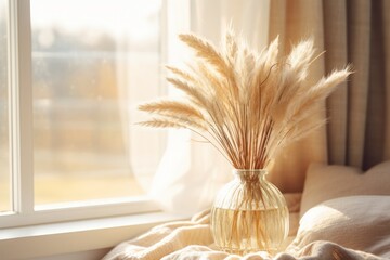 Dry pampas grass flowers in a glass vase on a tablet on a coffee table next to a bed, beige colored pillows and cushions, boho style