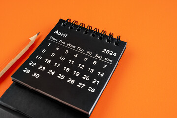 April 2024 desk calendar with pencil on orange background.