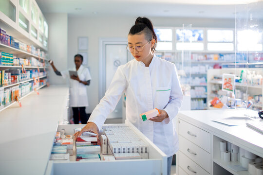 A focused pharmacist organizes medications with her colleague working in the background
