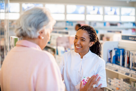 A young pharmacist joyfully assists an elderly woman at the drugstore