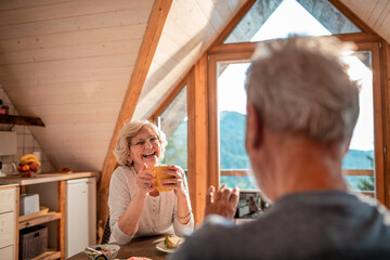 Senior woman laughing over morning coffee with her partner in a sunlit cabin