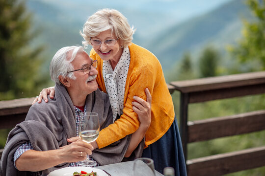 Loving senior couple hugging while having lunch on a cabin balcony - Powered by Adobe
