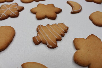 A white tablecloth filled with fresh homemade Christmas cookies in the shapes of snowflake, reindeer, moon, Christmas tree, Santa Claus and snowman. Festive wallpaper and background. Cozy scene.