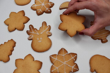 A hand picks up a cookie in the shape of a snowflake or star. There are Christmas cookies scattered...