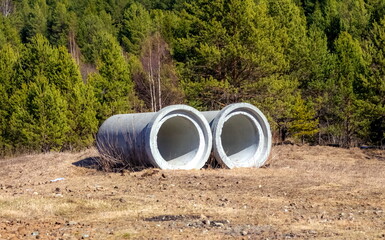 Large diameter concrete pipes in close-up against the background of trees in spring