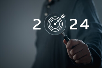Businessman hand holding magnifying glass with the year 2024 target darts 2024 business target plan...
