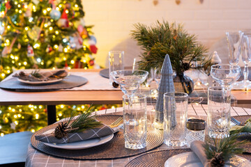 Serving a festive table with plates, forks, knives, napkins, glasses close-up in the modern interior of a loft house decorated for Christmas and New Year. Waiting for guests for a festive dinner