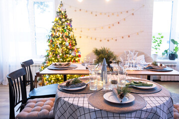 Serving a festive table with plates, forks, knives, napkins, glasses close-up in the modern interior of a loft house decorated for Christmas and New Year. Waiting for guests for a festive dinner