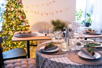 Festive interior of house is decorated for Christmas and New Year in loft style with black stove, fireplace, Christmas tree. Warm studio room with set table, burning wood, cozy and heating of home