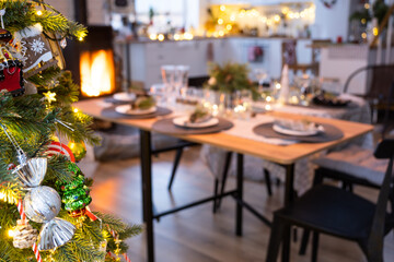 Serving festive table with plates, forks, knives, napkins, glasses close-up near stove fireplace in interior of loft house decorated for Christmas and New Year. Waiting for guests for festive dinner