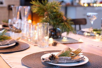 Serving a festive table with plates, forks, knives, napkins, glasses close-up in the modern interior of a loft house decorated for Christmas and New Year. Waiting for guests for a festive dinner