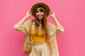 Smiling  carefree woman in straw hat and trendy summer linen  outfit  and posing on pink  background.  Vacation  and travel concept.