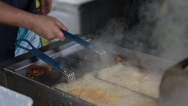Hand selects one of two baskets of fried chicken legs in a sizzling hot deep fryer