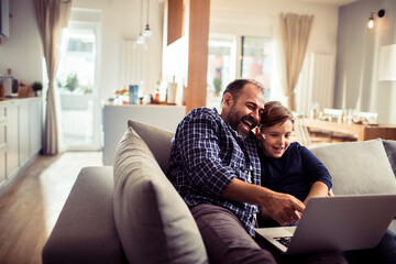 Young boy watching videos on the laptop with his dad on the sofa