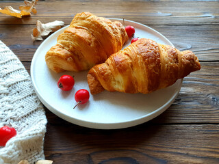 There is a plate with freshly baked croissants on the wooden table. Close-up.