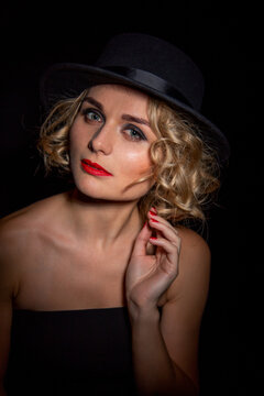 Sexy fashionable woman in an elegant hat and black dress. Mysterious blonde in retro style on a black.